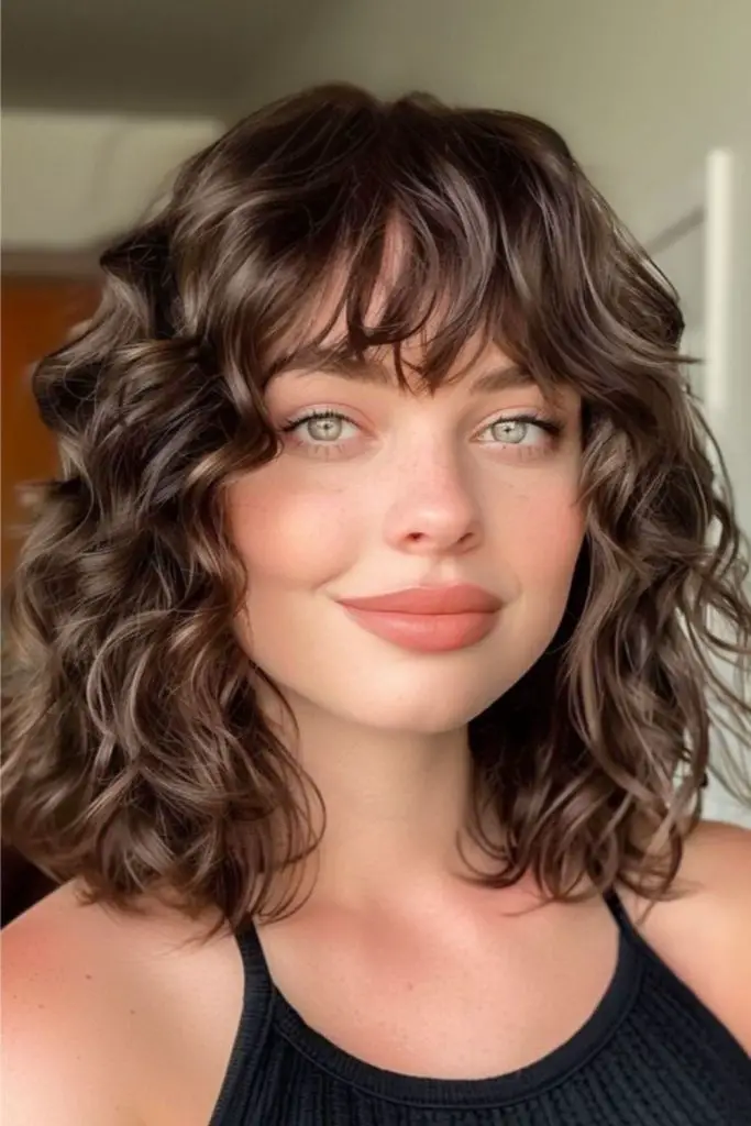 Soft bangs complement shoulder-length, natural curls.