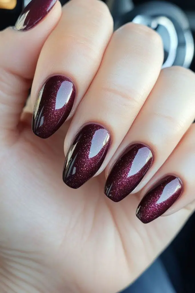 Glossy plum nails with glitter accents.