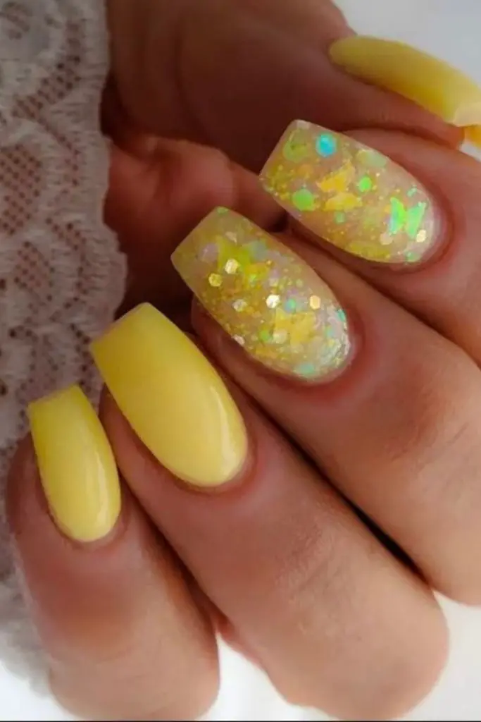 Confetti-tipped pastel yellow curved nails.