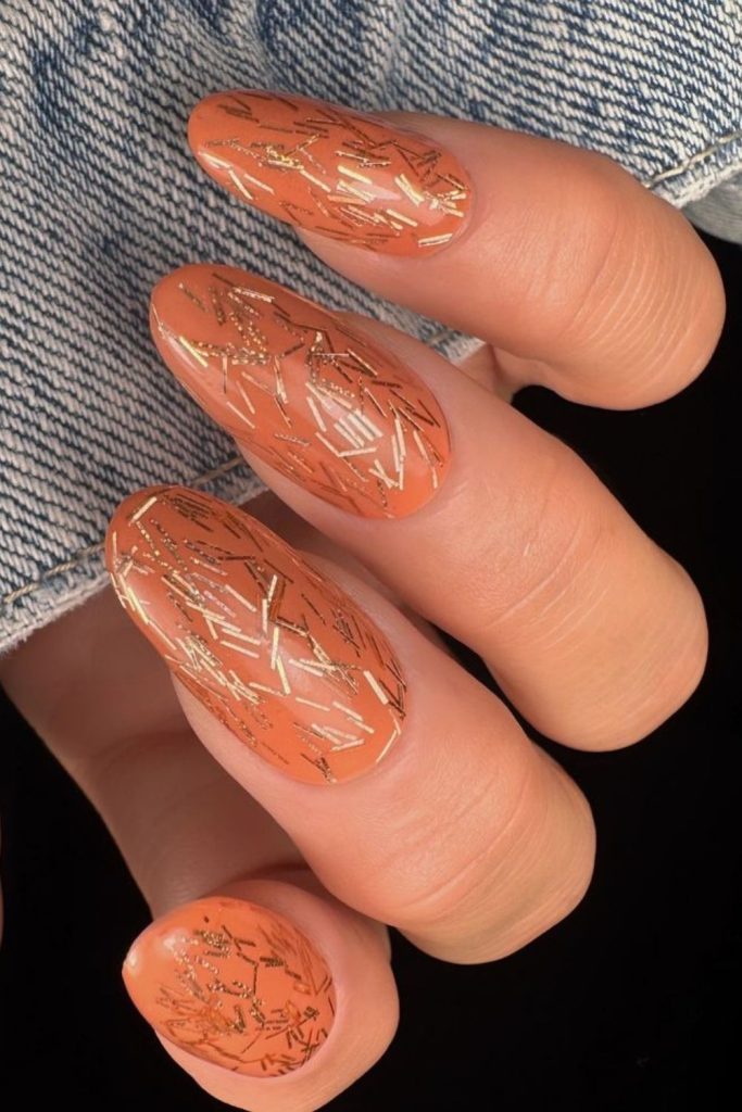 Coral nails with glowing gold flecks.